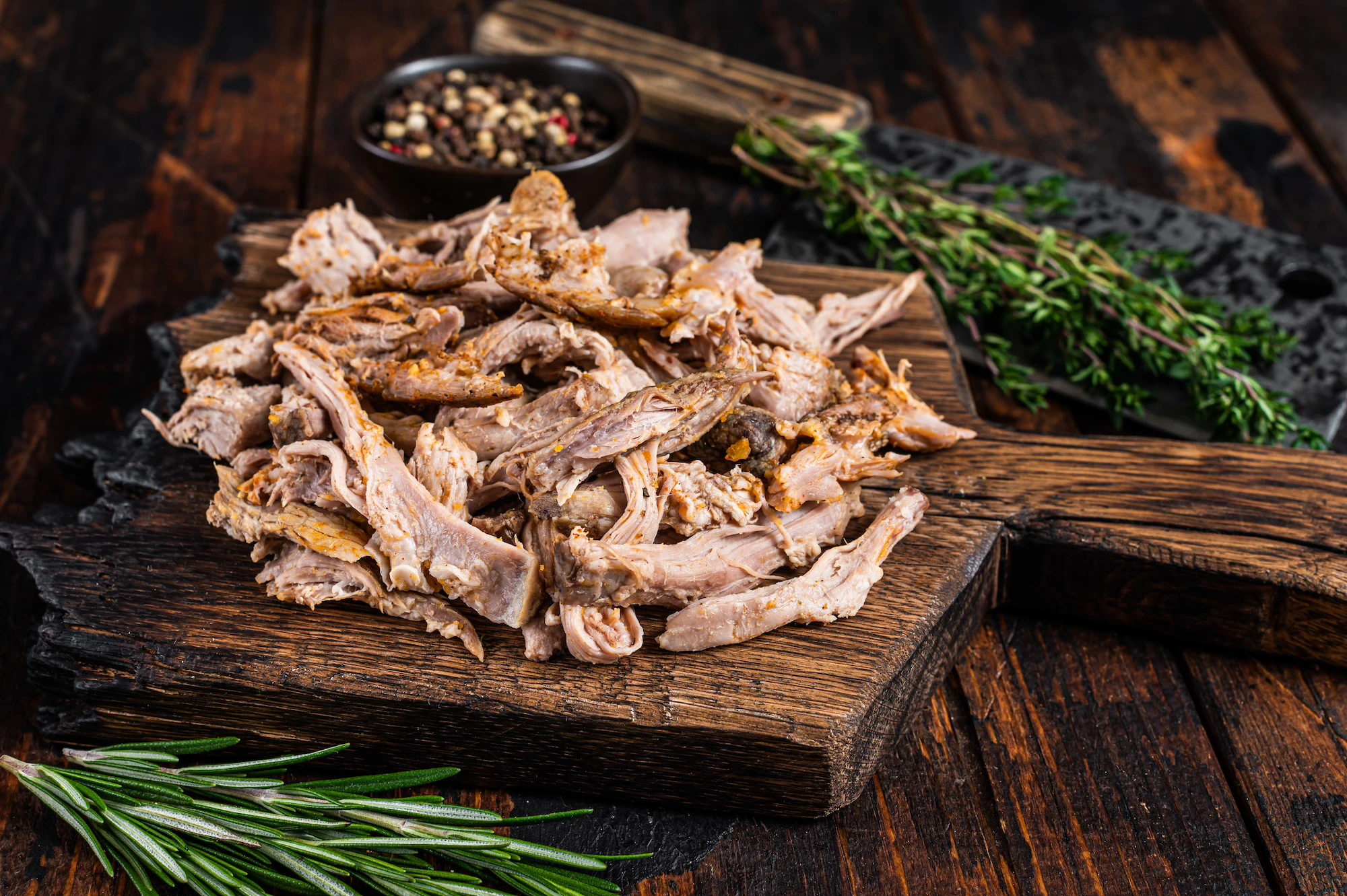 Slow cooked pulled pork meat on a wooden board with herbs and spices